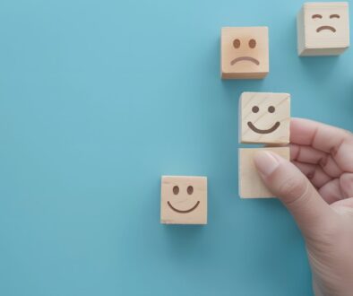 Hand choosing a happy face wooden block from a set of emojis on a blue background.